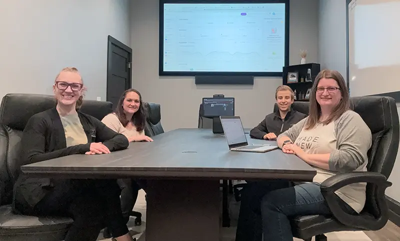 4 people sitting at a conference room table smiling at the camera